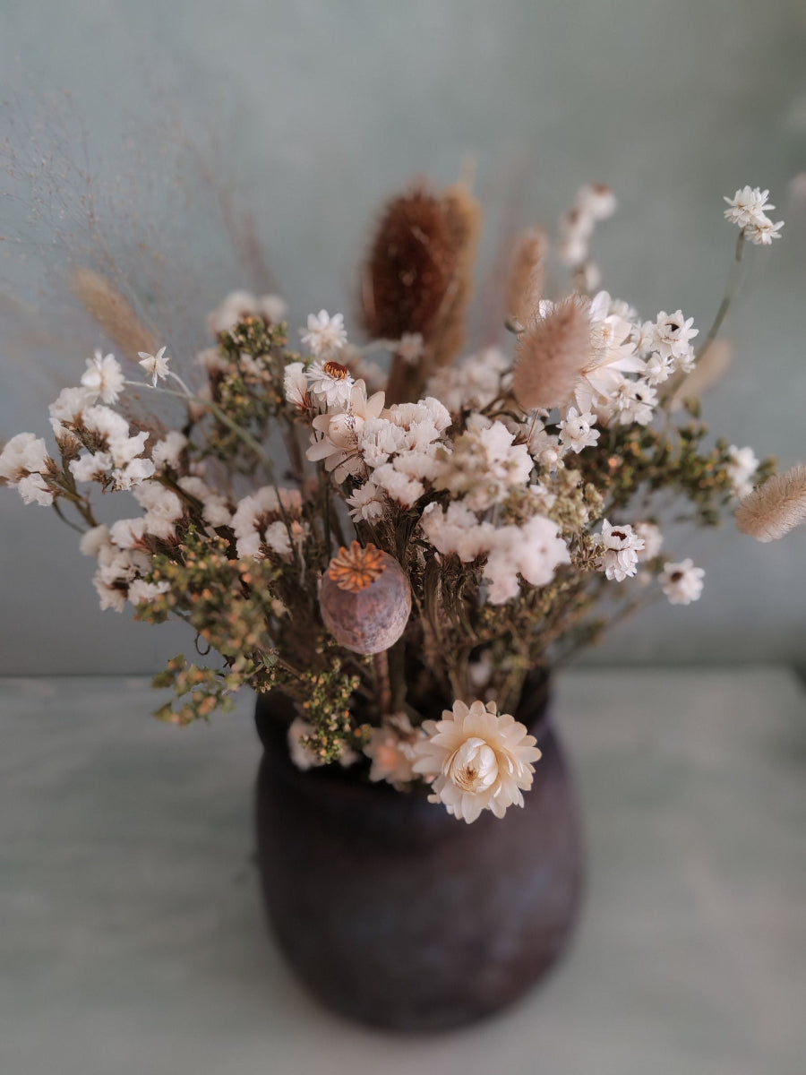 A rustic vase with bouquet of Irish dried flowers in whites greens and browns